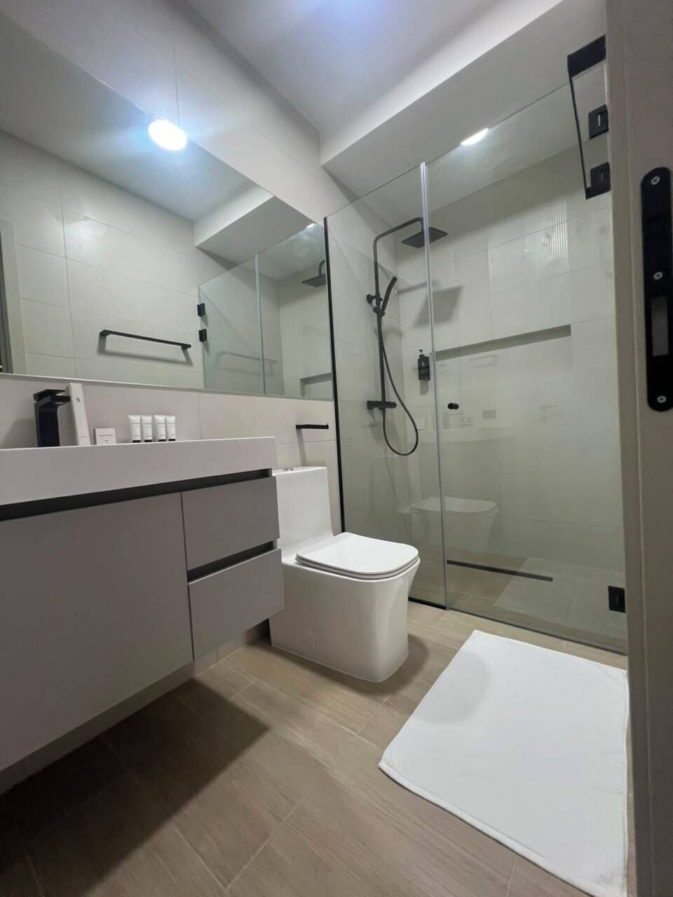 Une salle de bain moderne avec une douche à parois de verre, des toilettes blanches et un meuble-lavabo avec un miroir.