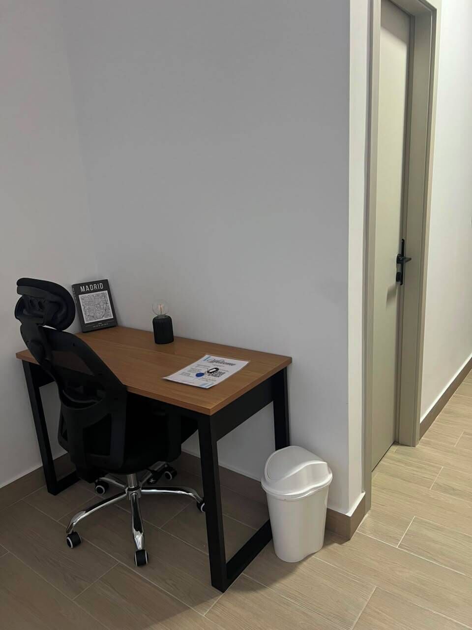 Ein kleiner Büroraum mit Schreibtisch, Stuhl, gerahmtem Bild und Papierkorb.