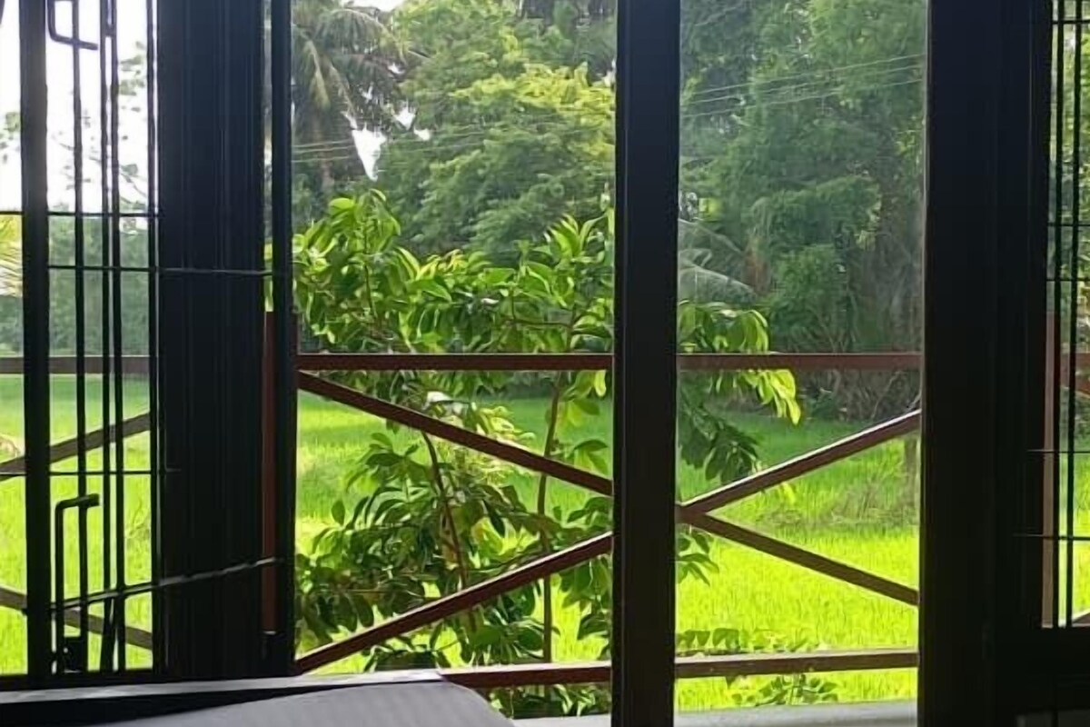 A room with a bed, a large window with a view of a green landscape, and a metal railing.