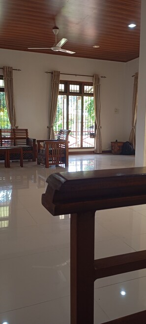 A room with a ceiling fan, large windows with curtains, wooden furniture, and a tiled floor. - Serene Rajarata (Anuradhapura)