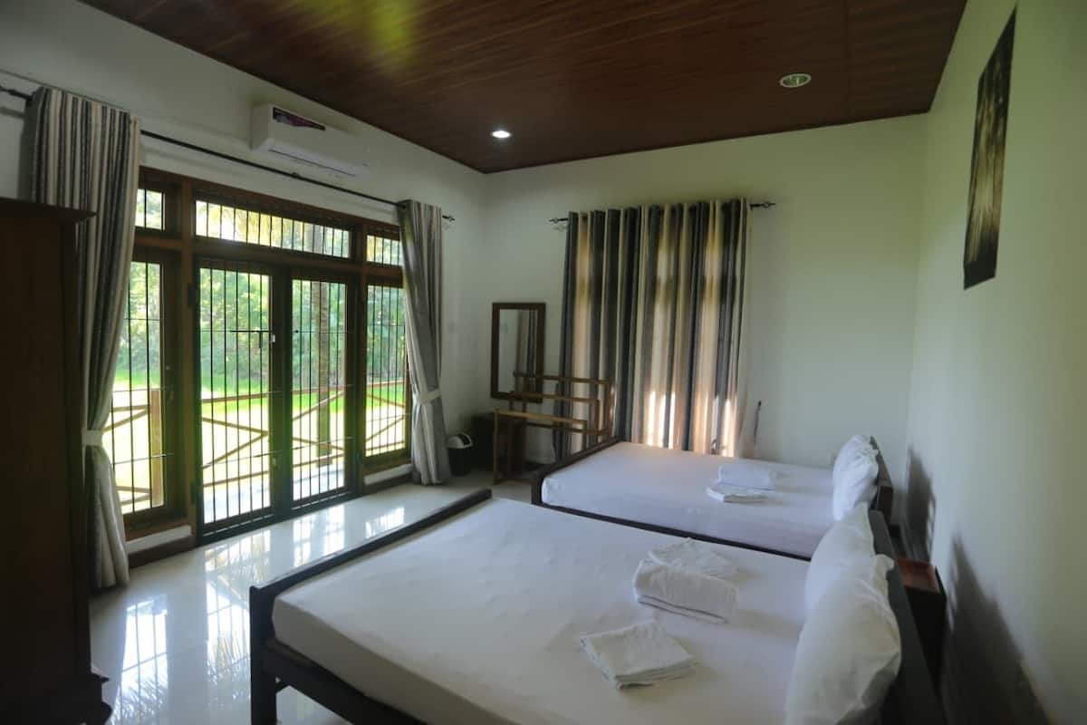 A hotel room with two beds, a large window with curtains, a ceiling fan, and an air conditioning unit.