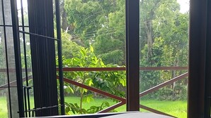 Une chambre avec un lit, une fenêtre donnant sur un paysage verdoyant et une rambarde en métal.