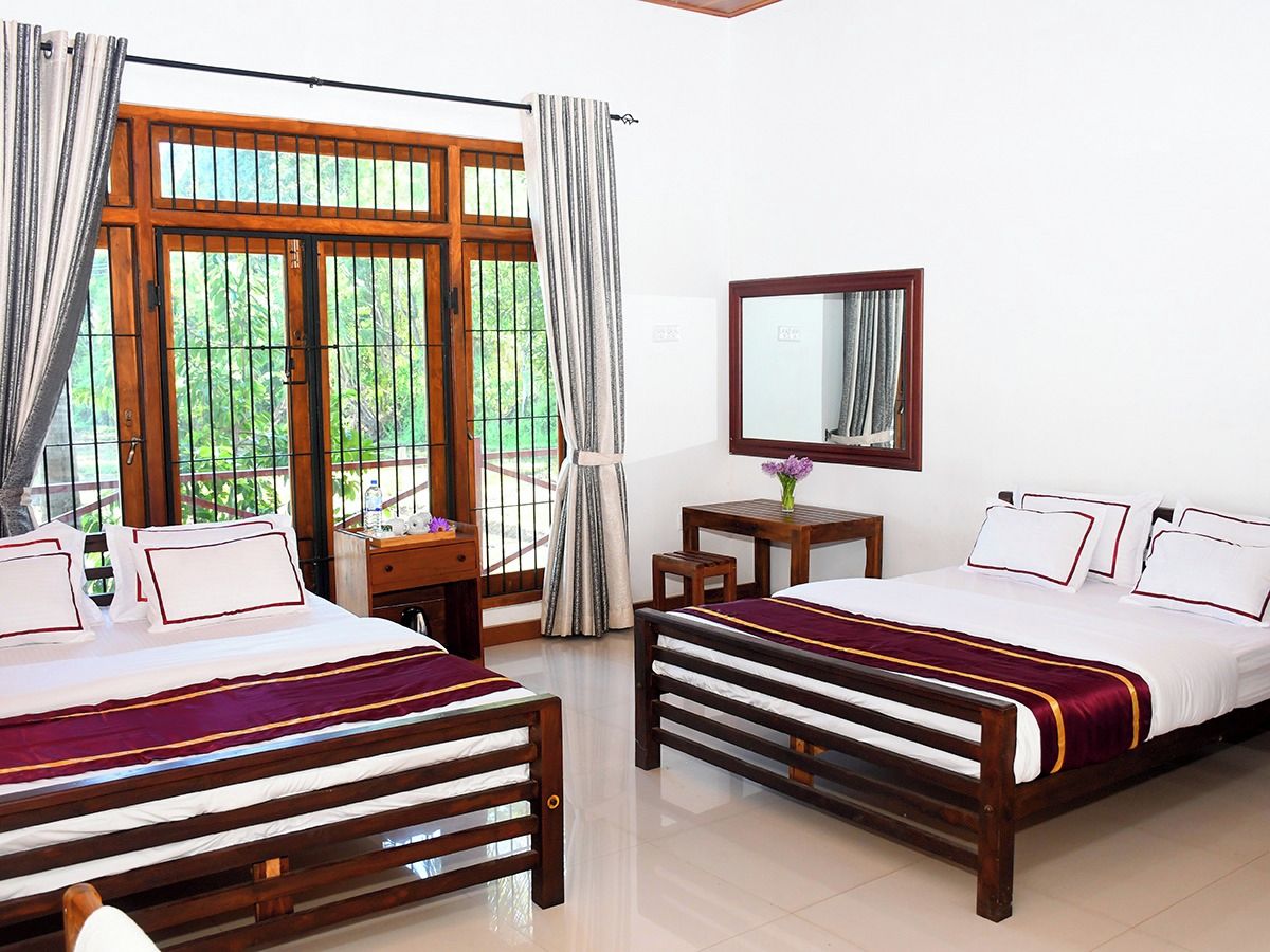 A hotel room with two beds, a desk, a chair, a mirror, and a window with curtains.