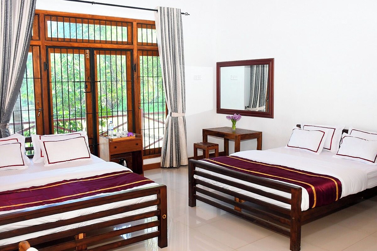 A hotel room with two beds, a desk, a chair, a mirror, and a window with curtains.