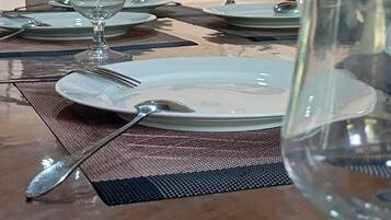 Una mesa de comedor dispuesta con platos, cubiertos y una copa de vino, con un ventilador de techo en lo alto.