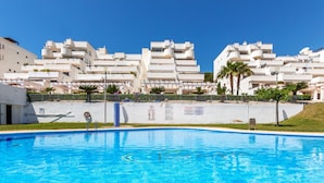Una piscina con superficie d'acqua cristallina e azzurra, circondata da un edificio bianco con numerosi balconi e un tetto piatto.