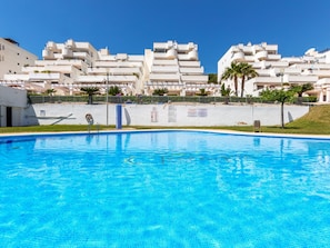 A swimming pool with a clear blue water surface, surrounded by a white building with multiple balconies and a flat roof. - Sunlight by Interhome (Peñiscola)