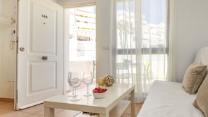 Una camera d'albergo con un letto, un tavolo con due bicchieri da vino e una ciotola di frutta, una porta con il numero 145 e vista sugli edifici attraverso tende leggere.