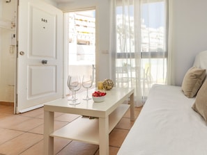 A hotel room with a bed, a table with two wine glasses and a bowl of fruit, a door with the number 145, and a view of buildings through sheer curtains. - Sunlight by Interhome (Peñiscola)
