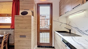 A modern kitchen with wooden cabinets, a built-in dishwasher, and a view through a glass door. - Le Pramecou (Val Claret) by Interhome (Tignes)