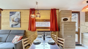 A dining area with a table set for four, wooden walls, a sofa, and a polar bear painting. - Le Pramecou (Val Claret) by Interhome (Tignes)