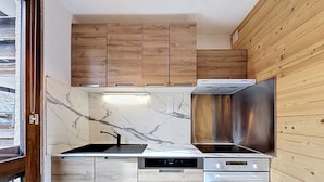 A compact kitchen with wooden cabinets, a stainless steel range hood, a built-in oven, and a marble backsplash. - Le Pramecou (Val Claret) by Interhome (Tignes)