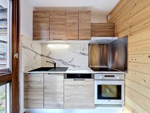 Eine kleine Küche mit Holzausstattung, einer Edelstahl-Dunstabzugshaube, einem Einbauofen und einer Marmor-Spritzschutzwand.