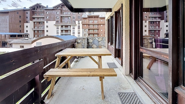 A balcony with wooden tables and a stone wall, overlooking a mountain and residential buildings. - Le Pramecou (Val Claret) by Interhome (Tignes)