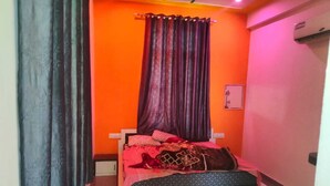Una habitación pequeña y de colores vivos, con una cama, una cortina y un aire acondicionado instalado en la pared.