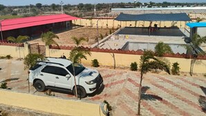 Un edificio con techo rojo, un espacio al aire libre cubierto y un aparcamiento asfaltado con un coche blanco.