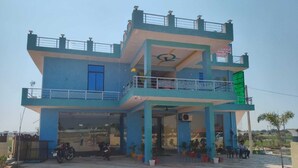 Un edificio de dos pisos con un balcón, una entrada cubierta y un área de estacionamiento con motocicletas.