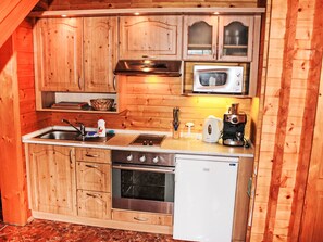 Eine kleine Küche mit Holzschränken, einem Edelstahl-Spülbecken, einer Mikrowelle, einer Kaffeemaschine und einem Kühlschrank.