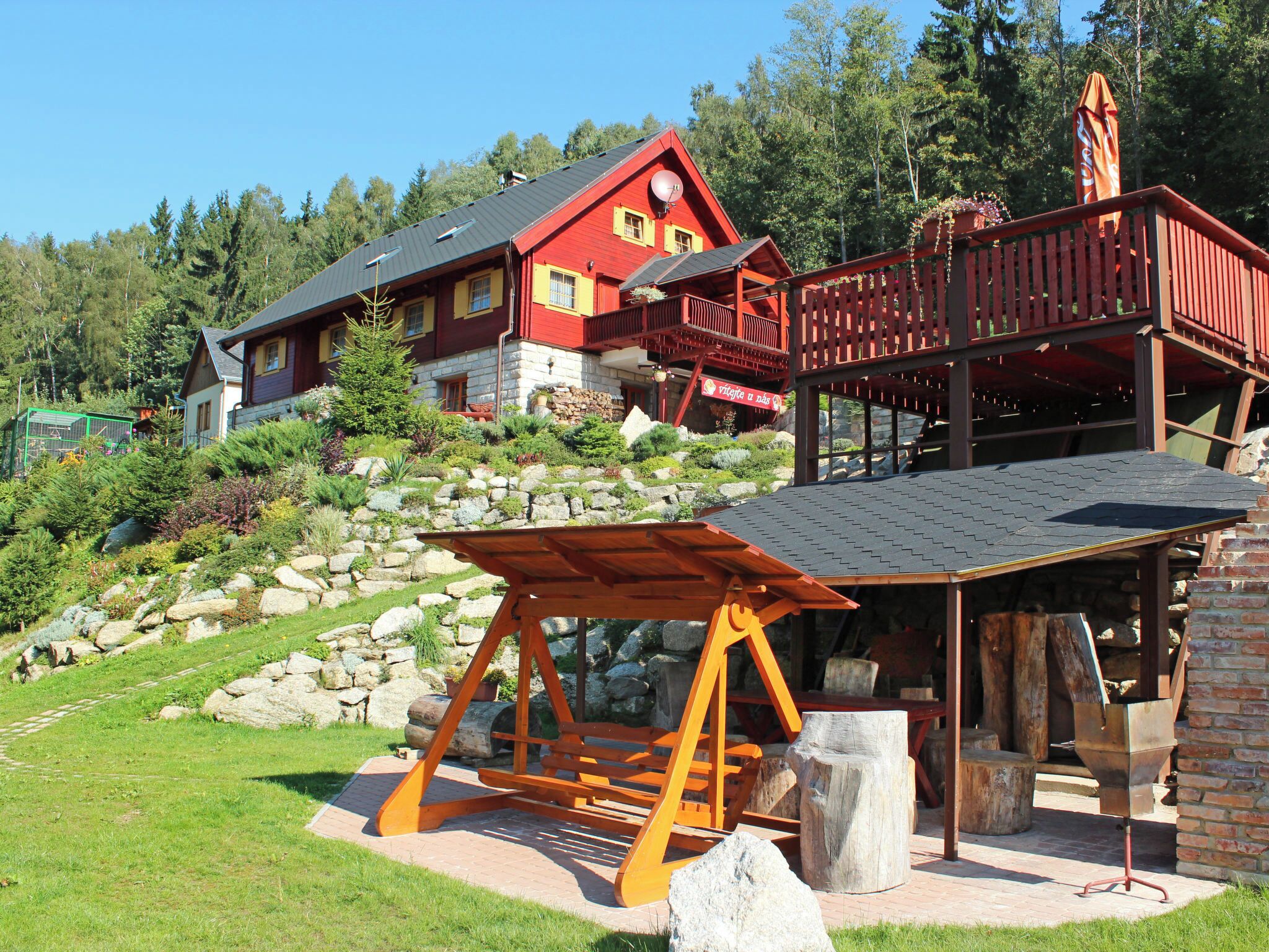 A red building with a balcony, surrounded by greenery and a stone wall.