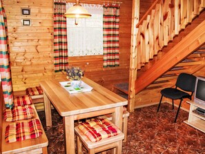 Ein Holzinnenraum mit einer Holztreppe, einem Esstisch mit Bänken, einem Fernseher und einem Fenster mit Vorhängen.