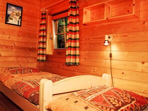 Ein Holzhütten-Zimmer mit zwei Betten, einem Fenster und einer Wandleuchte.