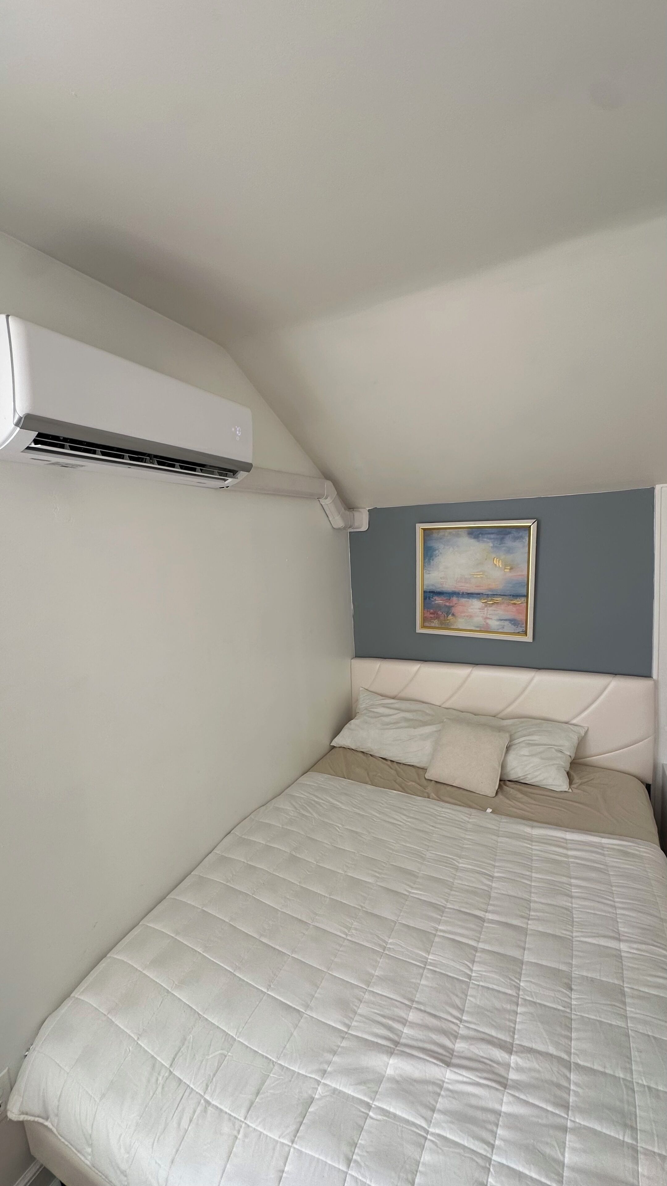 Ein Schlafzimmer mit einem Bett, einem Gemälde und einer Klimaanlage.