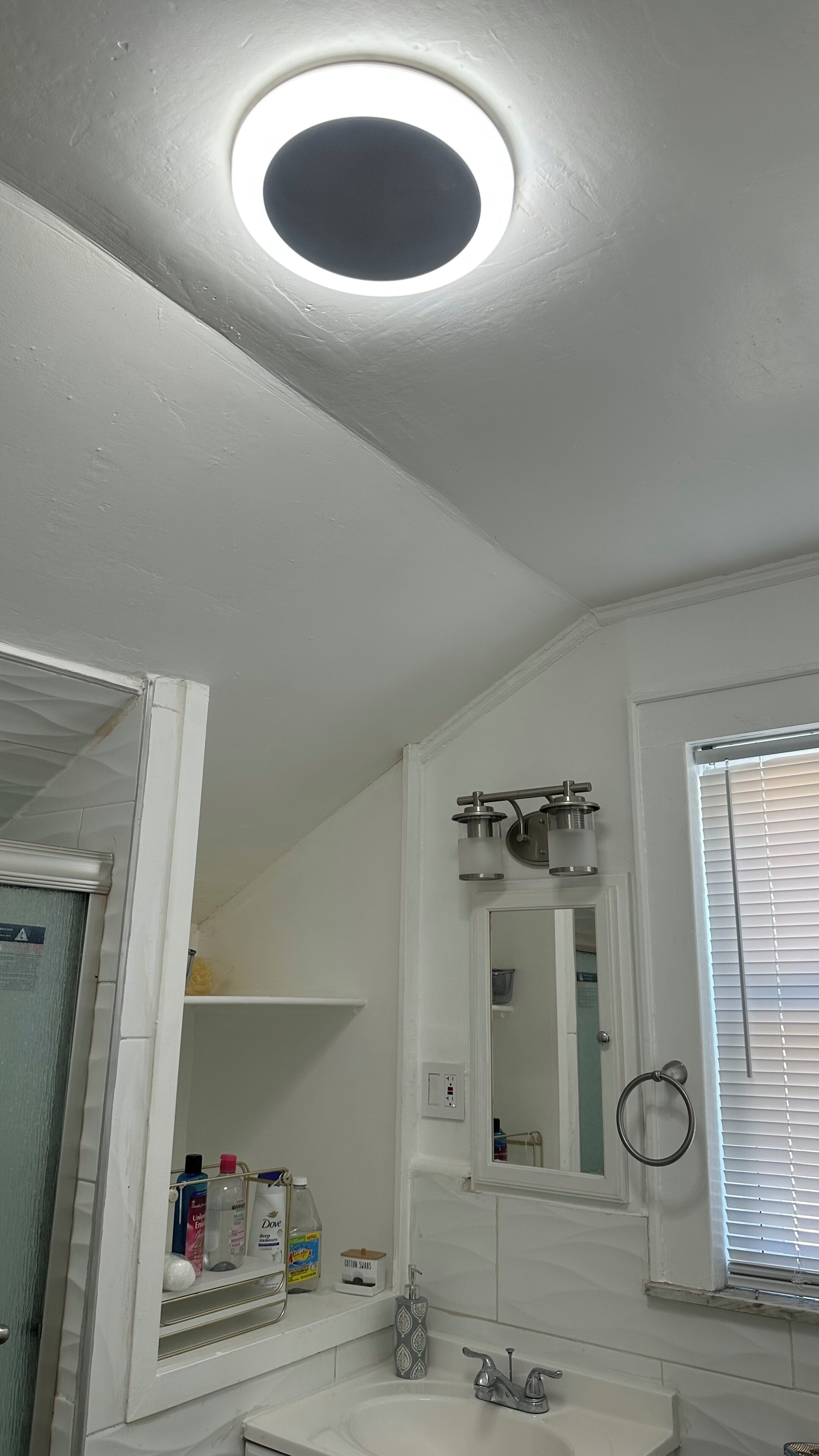 Ein Badezimmer mit weißem Waschbecken, einem Spiegel, einem Handtuchhalter und einem Fenster mit Jalousien.