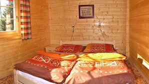 Ein Zimmer in einer Holzhütte mit einem Bett, einem Fenster mit Vorhängen und einem gerahmten Bild an der Wand.