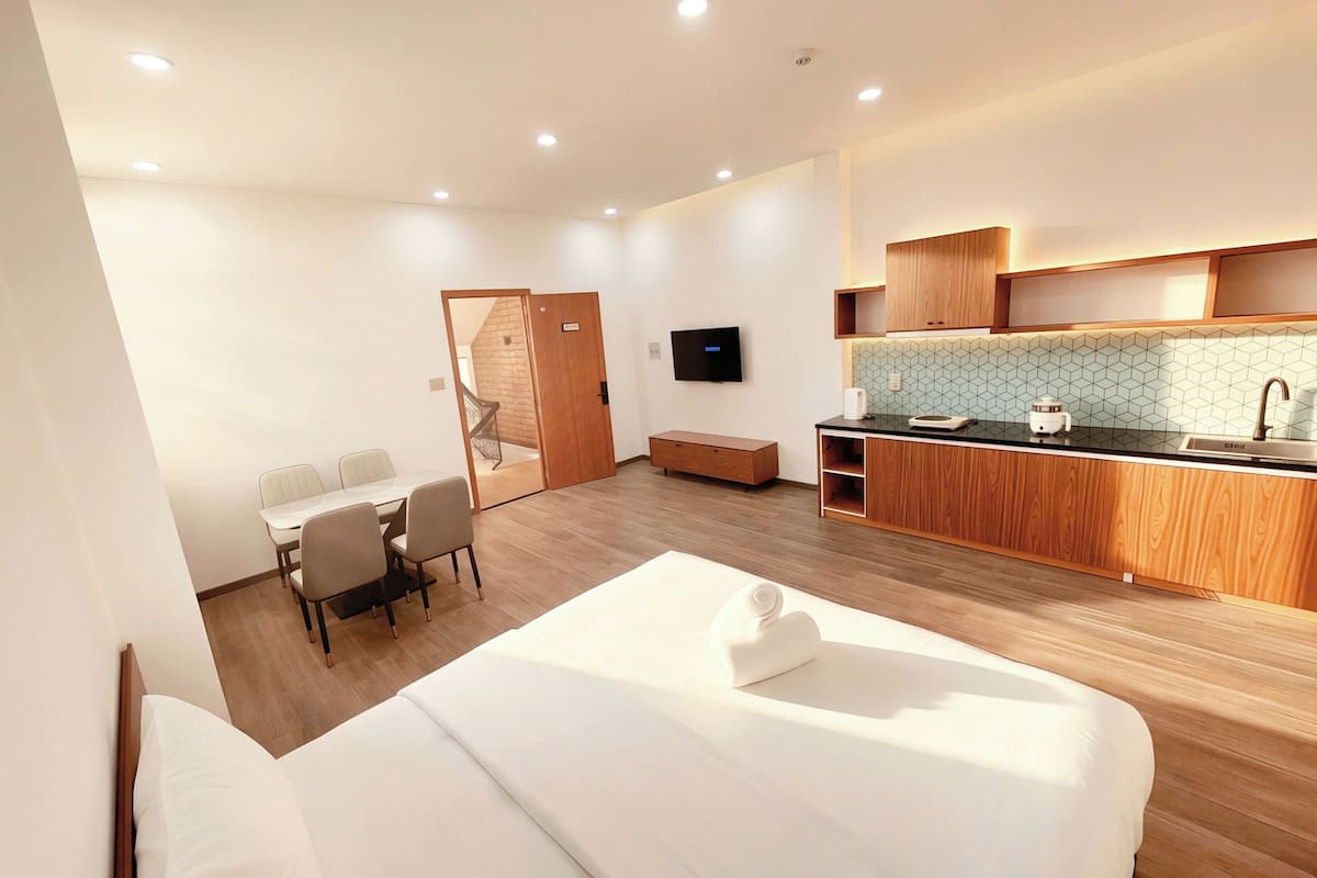 Una habitación de hotel moderna con cama, una pequeña mesa de comedor, kitchenette y televisión.