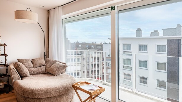 Een moderne woonkamer met een groot raam, een ronde bank, een houten bijzettafeltje en een vloerlamp.