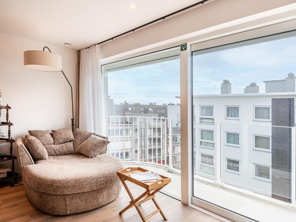 Ein modernes Wohnzimmer mit großem Fenster, einem runden Sofa, einem Holztisch und einer Stehlampe.