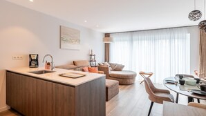 Een moderne keuken met een centraal eiland, een eethoek met een ronde tafel en een zithoek met een bank en voetenbankje.
