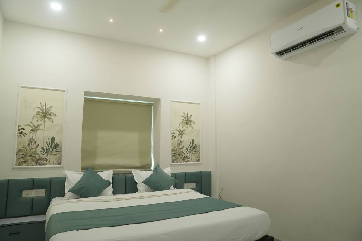 A bedroom with a bed, a nightstand, a wall-mounted air conditioner, and two framed botanical prints.