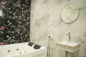 A modern bathroom with a marble wall, a geometric tile backsplash, a freestanding bathtub, and a pedestal sink with a decorative border. - Hotel South Square (Nagpur)