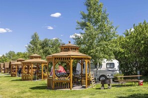 A campground with wooden gazebos, picnic tables, and a white RV.