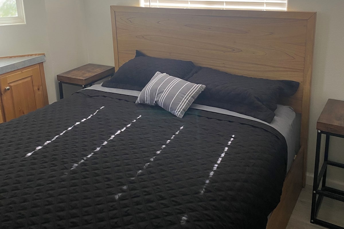 A bedroom with a bed, a window with blinds, a wooden headboard, and a nightstand.