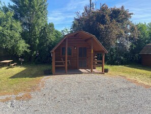 A wooden cabin with a porch, a picnic table, and a gravel driveway.