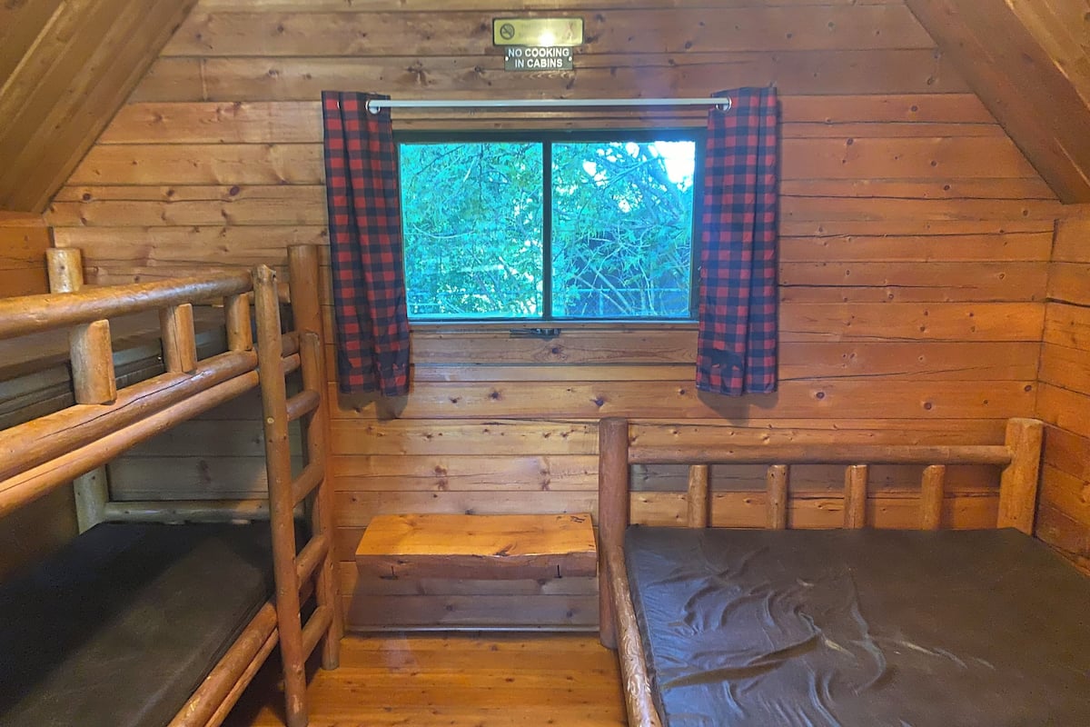 A cabin with wooden walls, a window with checkered curtains, and a bunk bed.