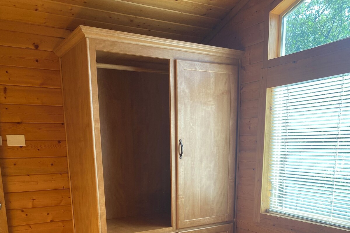 Un dormitorio de madera con cama, armario y ventana con persianas.