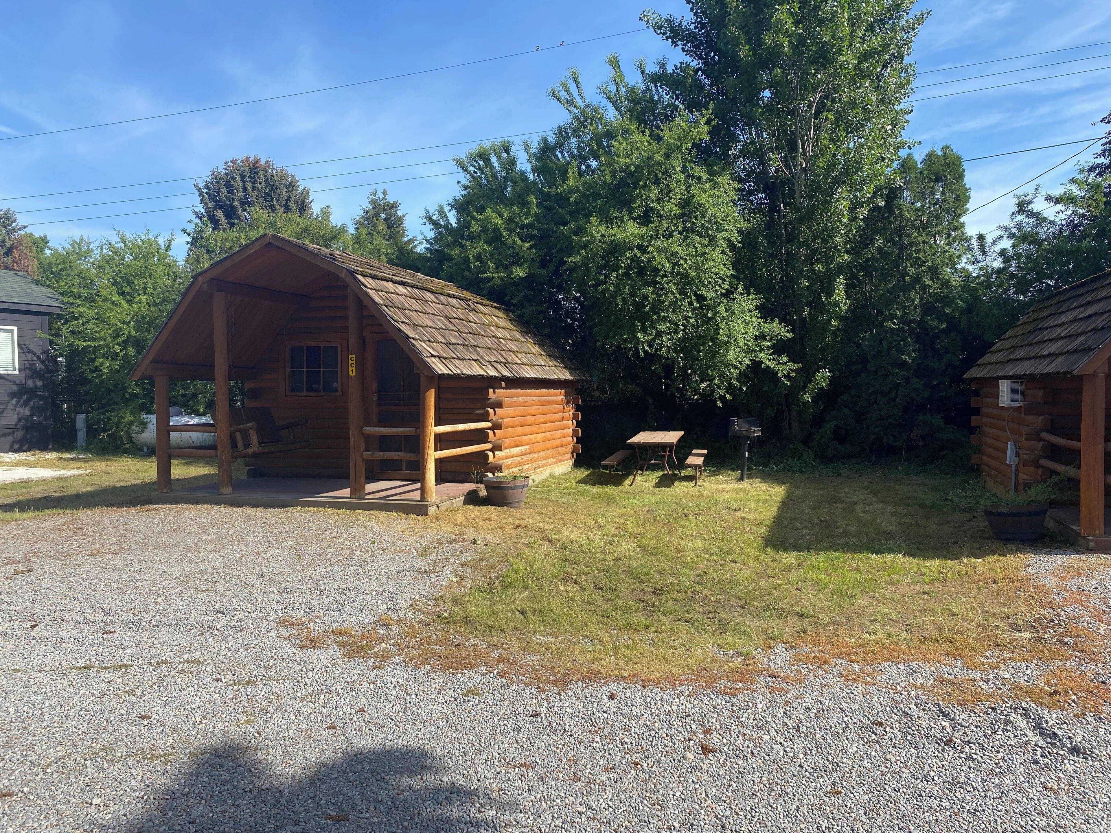 Une cabane rustique en rondins de bois, dotée d’une véranda, d’une table de pique-nique et d’un espace barbecue.