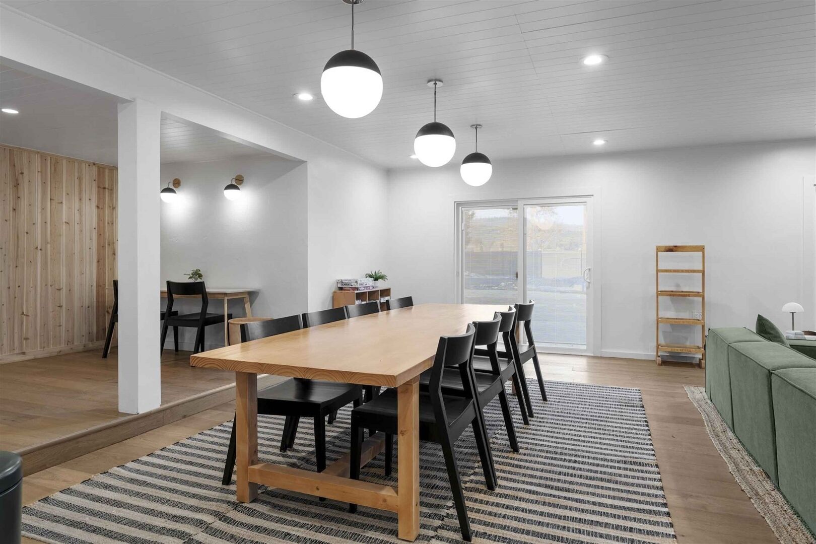 Een moderne eethoek met een houten tafel en stoelen, hanglampen en uitzicht door een glazen deur.