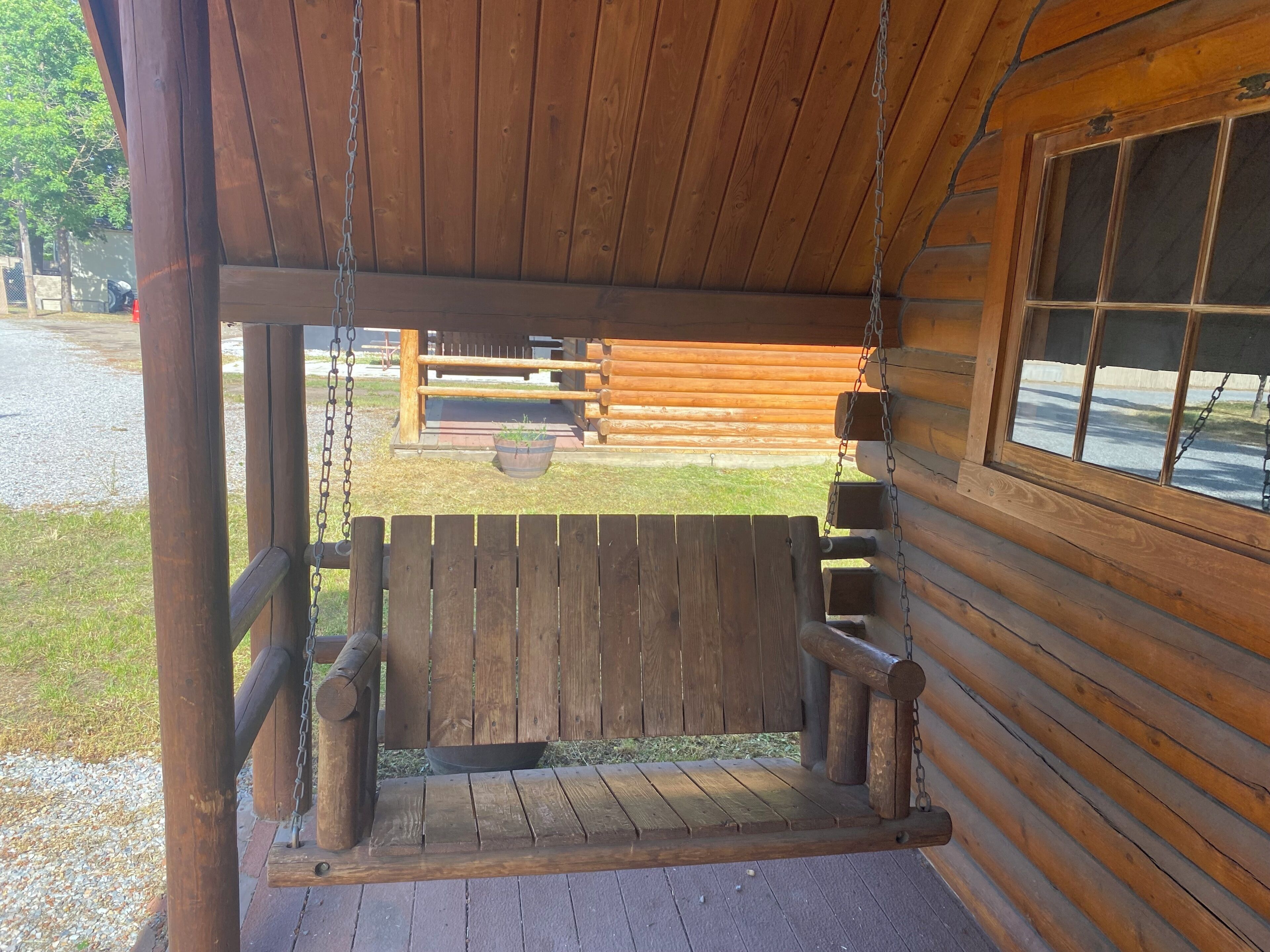 A wooden porch with a swing, a window, and a view of a grassy area.