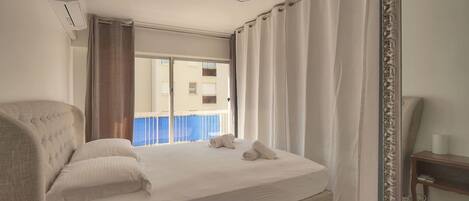 Une chambre d’hôtel avec un lit, une table de chevet, un miroir et une vue sur un immeuble par la fenêtre.