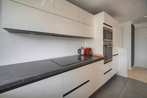 A modern kitchen with white cabinetry, a black countertop, and stainless steel appliances including a coffee maker and an oven. - Frgk Alexander III Elegant 1-Bedroom Apartment with Terrace in Palm Beach (Cannes)