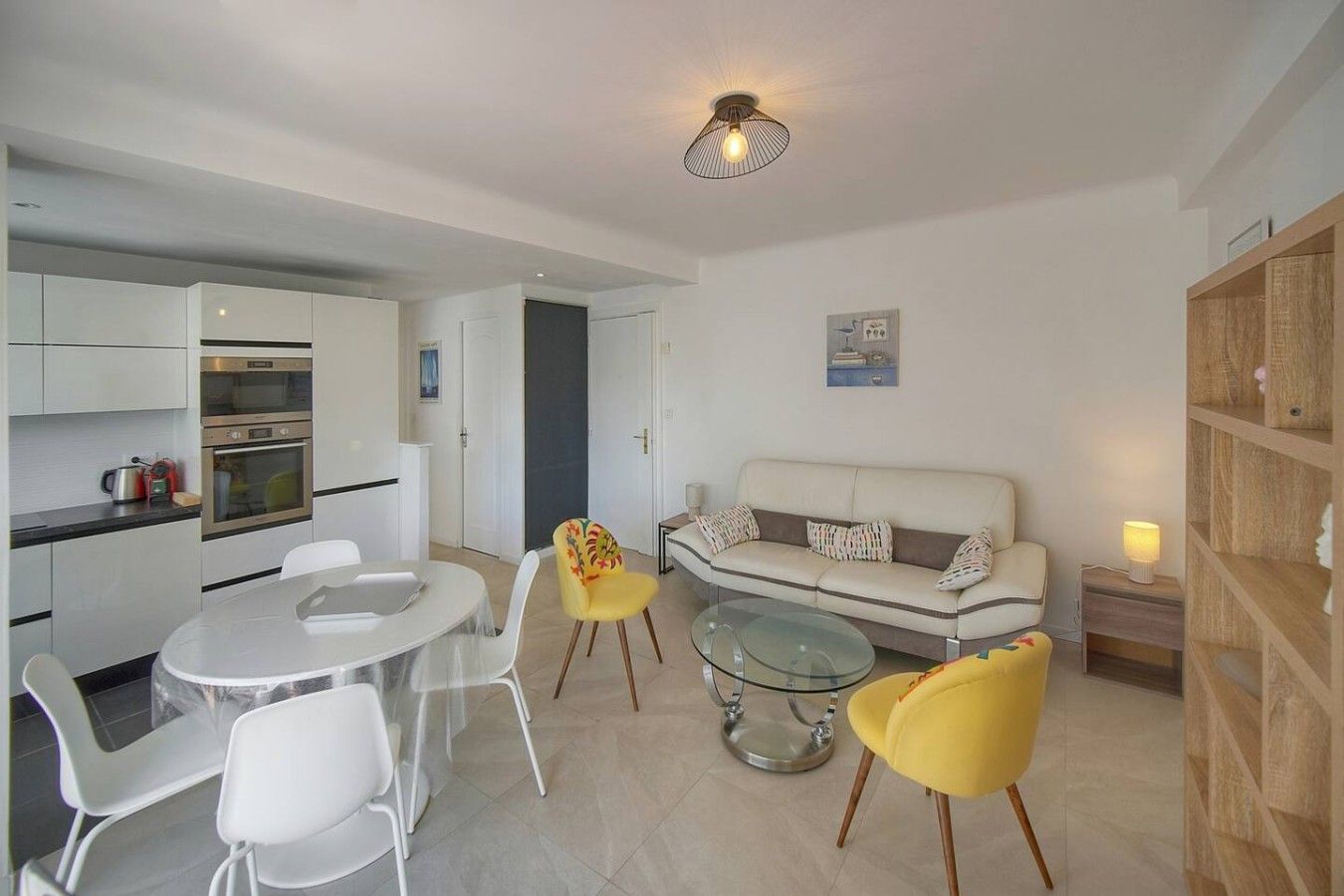 A compact living space with a kitchenette, a dining area with a glass table, and a seating area with a sofa and chairs.