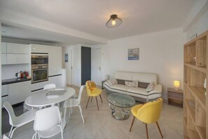 A compact living space with a kitchenette, a dining area with a glass table, and a seating area with a sofa and chairs. - Frgk Alexander III Elegant 1-Bedroom Apartment with Terrace in Palm Beach (Cannes)