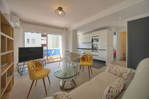 Ein modernes Wohnzimmer mit einem Glastisch, zwei gelben Sessel, einer Couch und einem Flachbildfernseher.