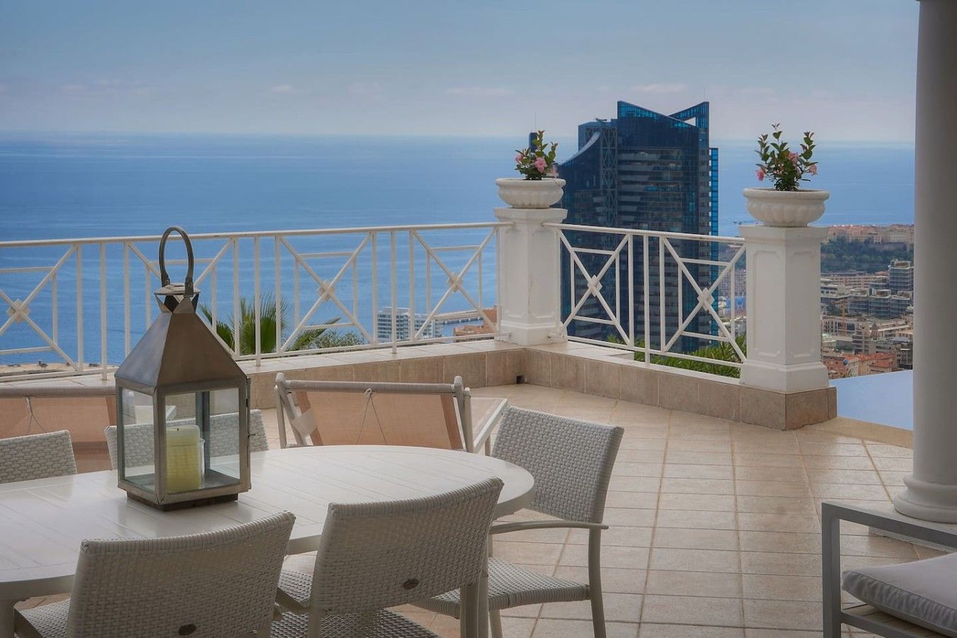 Une terrasse avec vue sur la mer, comprenant une table et des chaises, une lanterne et des plantes en pot.