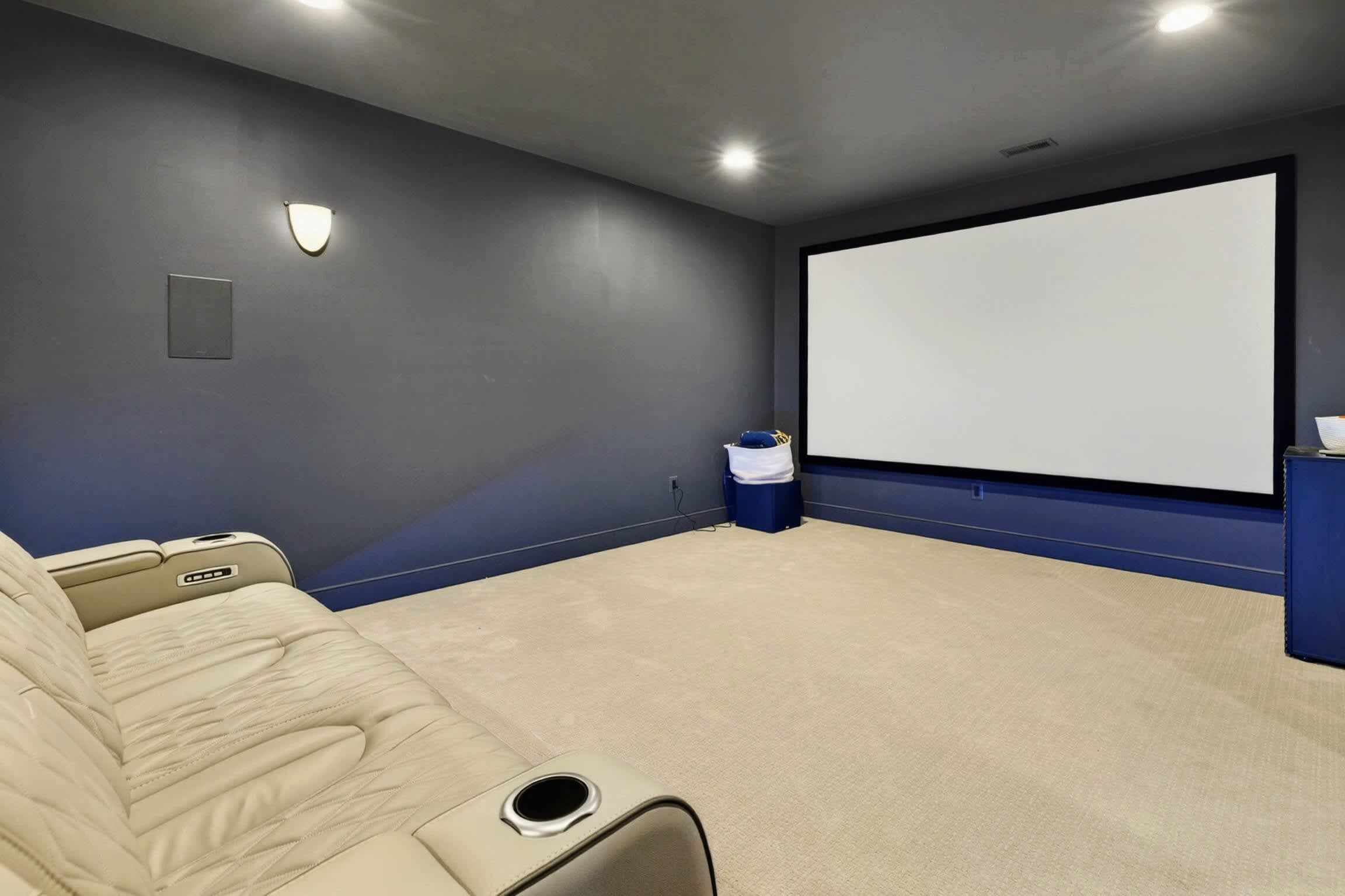 Sala de cinema com tela grande, poltrona reclinável e piso coberto por carpete.