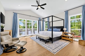Un dormitorio amplio con cama con dosel, ventilador de techo y ventanas grandes que ofrecen vistas a zonas verdes.